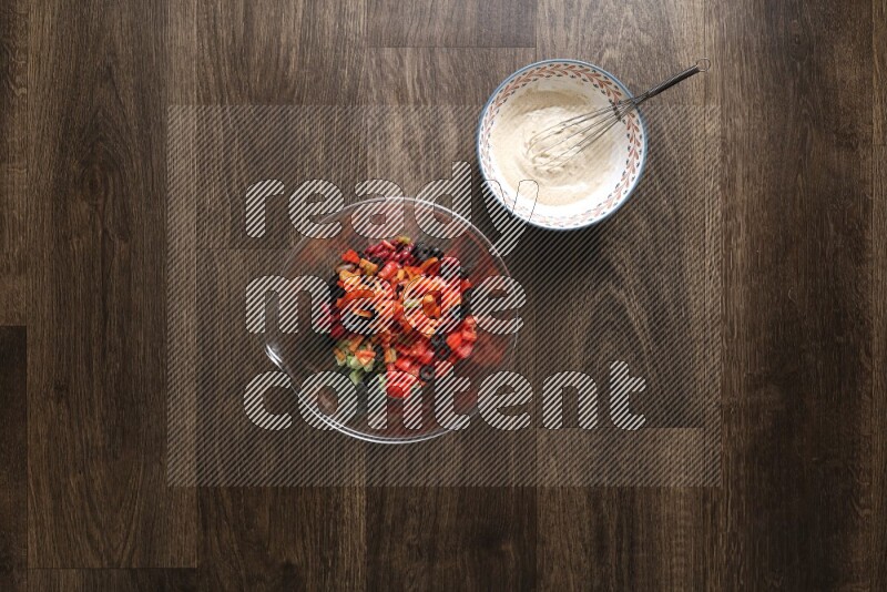 A bowl full of salad (avocado, tomatoes, red beans, olives, bell pepper, corn, lettuce) and bowl of salad dressing on wooden background