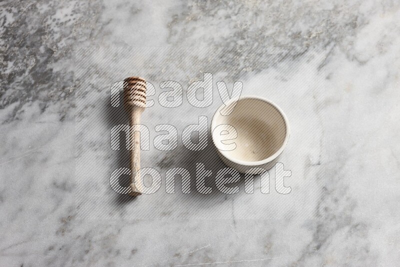White pottery bowl with wooden honey dipper on the side on grey marble background