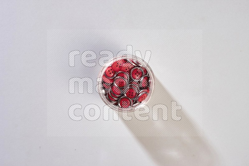 A glass jar full of colored buttons on grey background