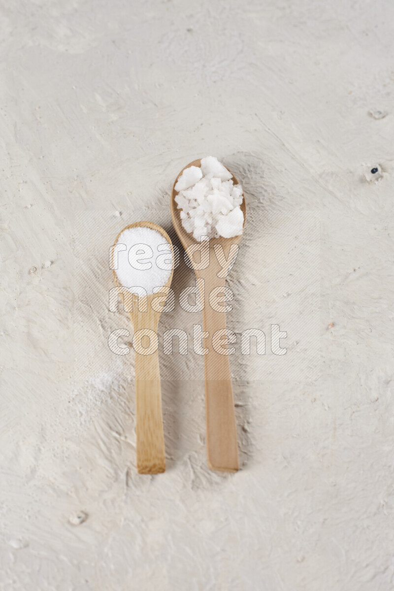 2 wooden spoons filled with fine and coarse salt on white background