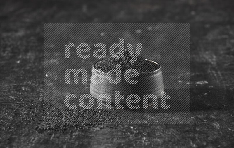 وعاء فخاري أسود ممتلئ ببذور حبة البركة علي خلفية سوداء