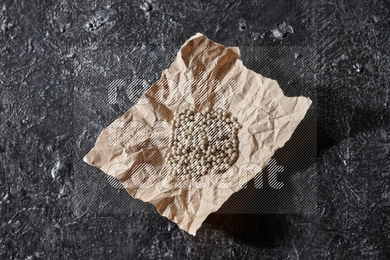 White pepper beads in a crumpled piece of on textured black flooring