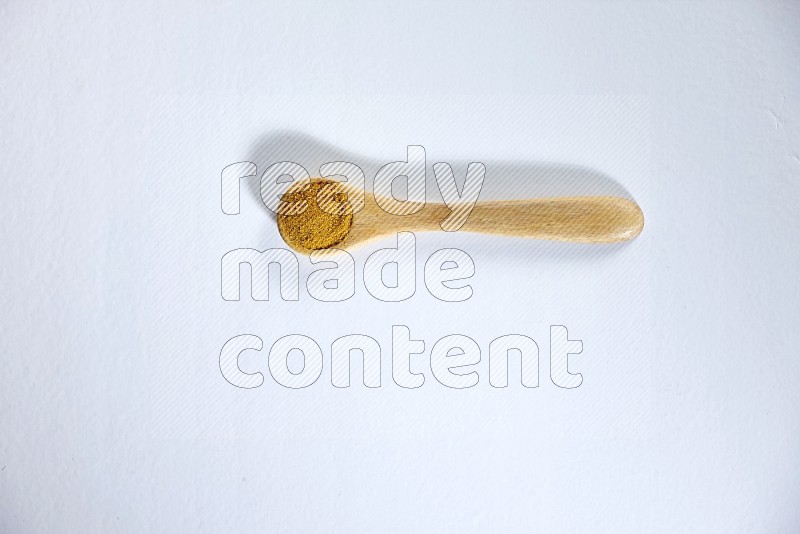 A wooden spoon full of turmeric powder on white flooring