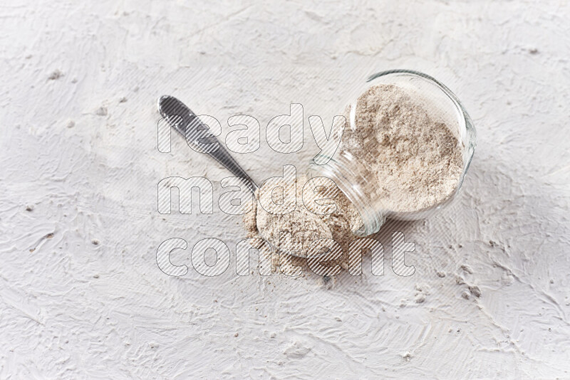 A glass jar full of onion powder flipped with some spilling powder on white background