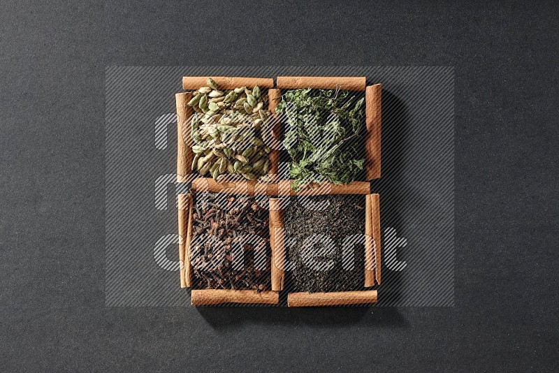 4 مربعات من عيدان القرفة ممتلئة بالشاي الأسود والقرنفل والنعناع المجفف وحبوب الهيل على أرضية سوداء