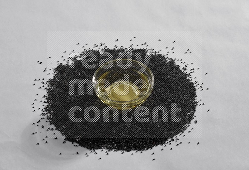 A glass bowl full of black seeds oil surrounded by the seeds on a white flooring