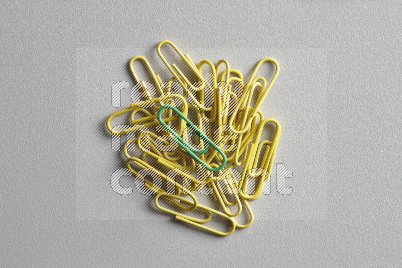 A green paperclip surrounded by bunch of yellow paperclips on grey background