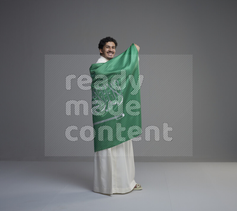 رجل سعودي يرتدي ثوب ابيض ويحمل علم السعودية