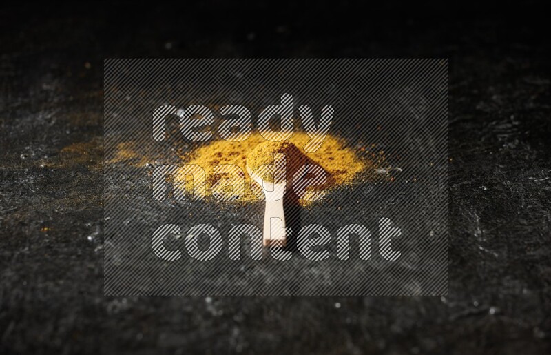 A wooden spoon full of turmeric powder on textured black background