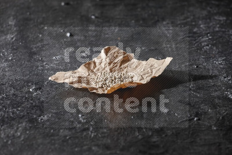 White pepper beads in a crumpled piece of on textured black flooring