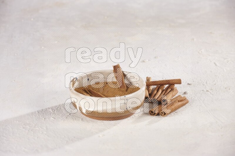 Ceramic bowl full of cinnamon powder with cinnamon sticks on the side on white background