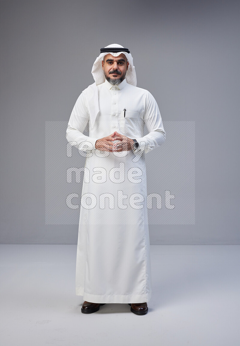 Saudi man Wearing Thob and white Shomag standing interacting with the camera on Gray background