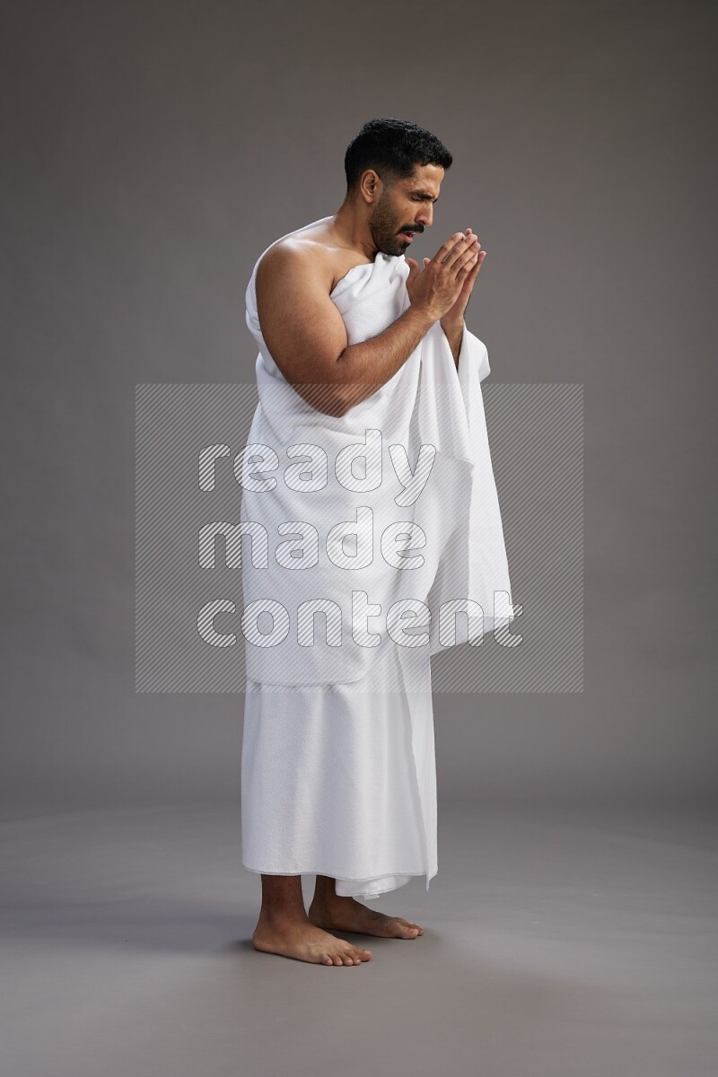A man wearing Ehram standing showing how to sneeze on gray background