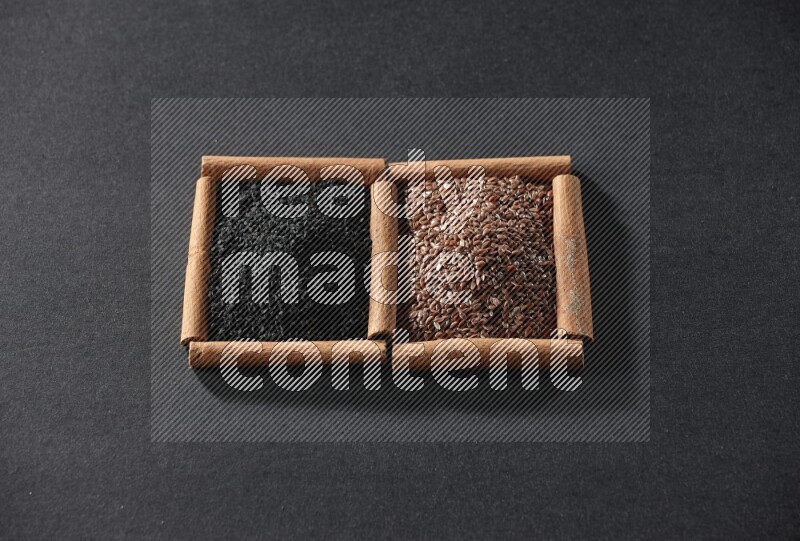 مربعان من أعواد القرفة ممتلئان ببذور الكتان وحبة البركة السوداء علي خلفية سوداء