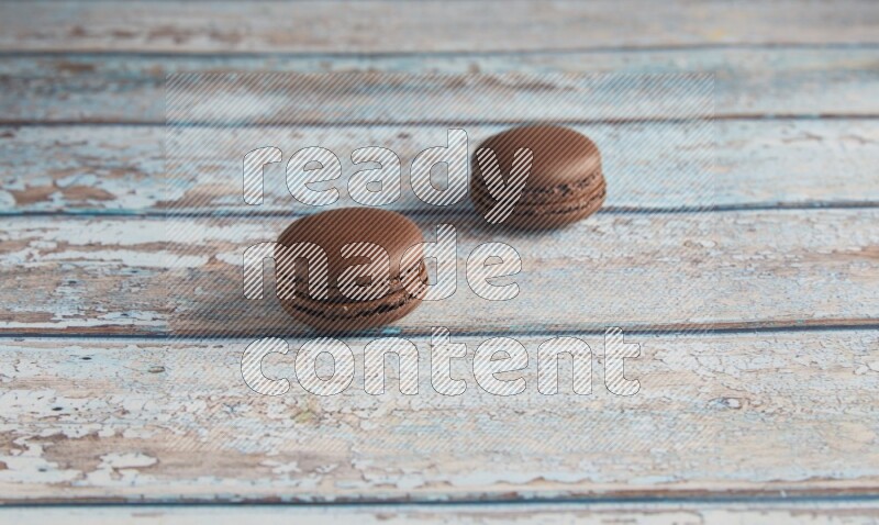45º Shot of two Brown Dark Chocolate macarons on light blue wooden background