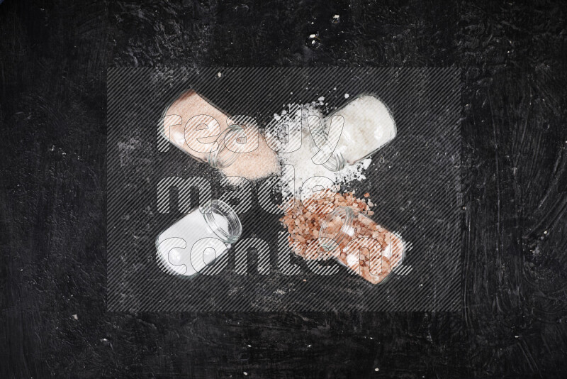 4 glass jars filled with table salt, coarse sea salt, fine himalayan salt and coarse himalayan salt on black background