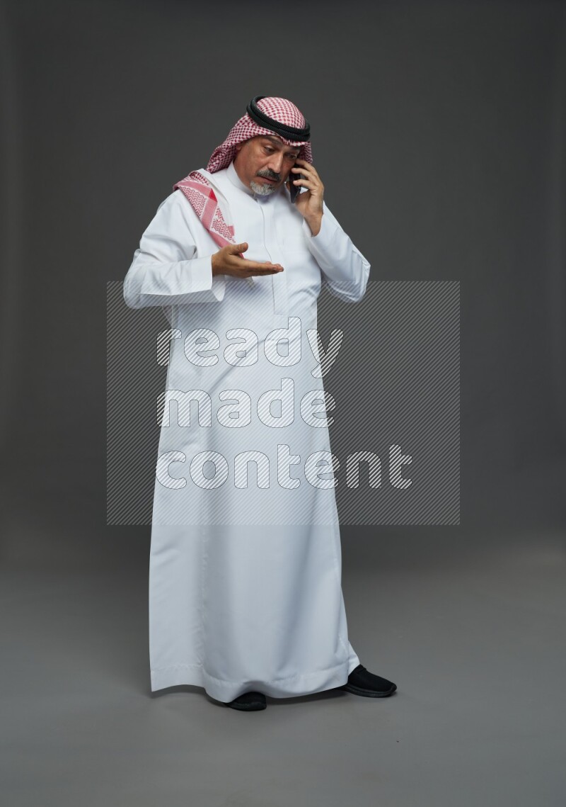 Saudi man with shomag Standing talking on phone on gray background