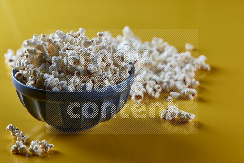 A blue pottery bowl full of popcorn with popcorn beside it on a yellow background in different angles