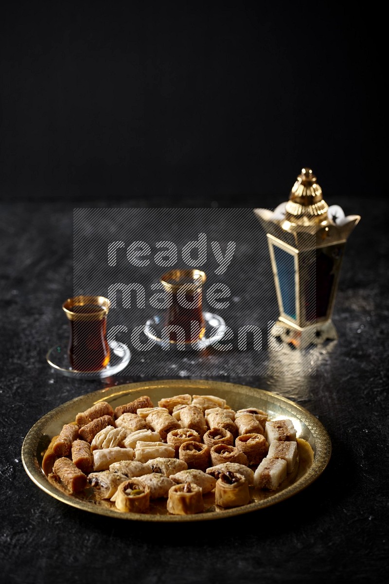 حلويات شرقية مع الشاي وفانوس معدني علي خلفية سوداء خشبية