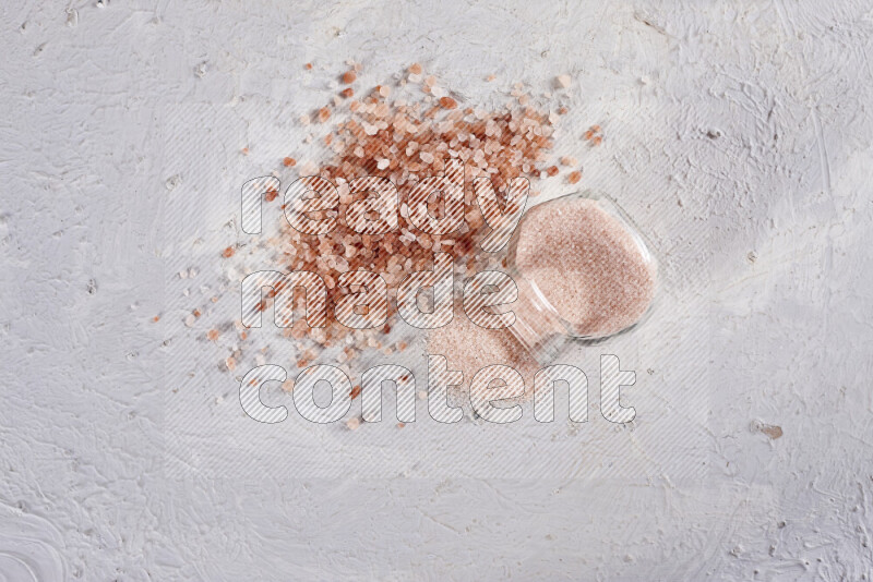 A glass jar full of fine himalayan salt with some himalayan crystals beside it on a white background