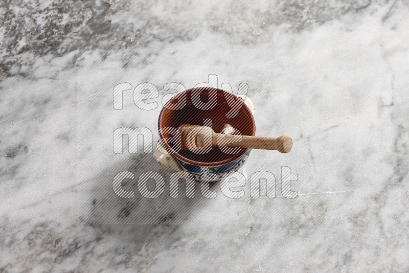 Decorative Pottery Pot with wooden honey handle in it, on grey marble flooring, 65 degree angle