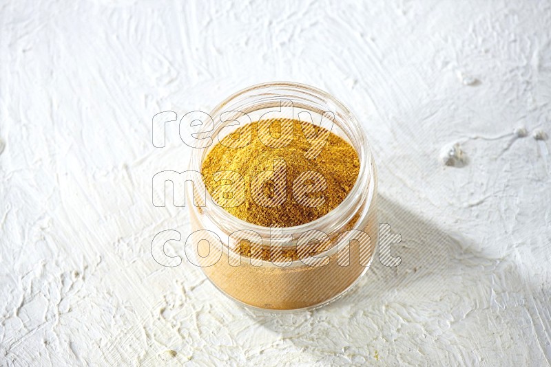 A glass jar full of turmeric powder on a textured white flooring