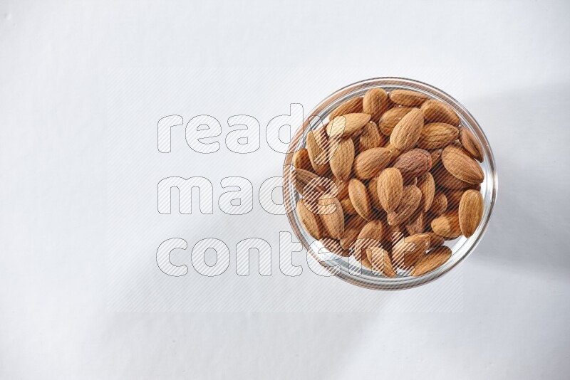 A glass bowl full of peeled almonds on a white background in different angles