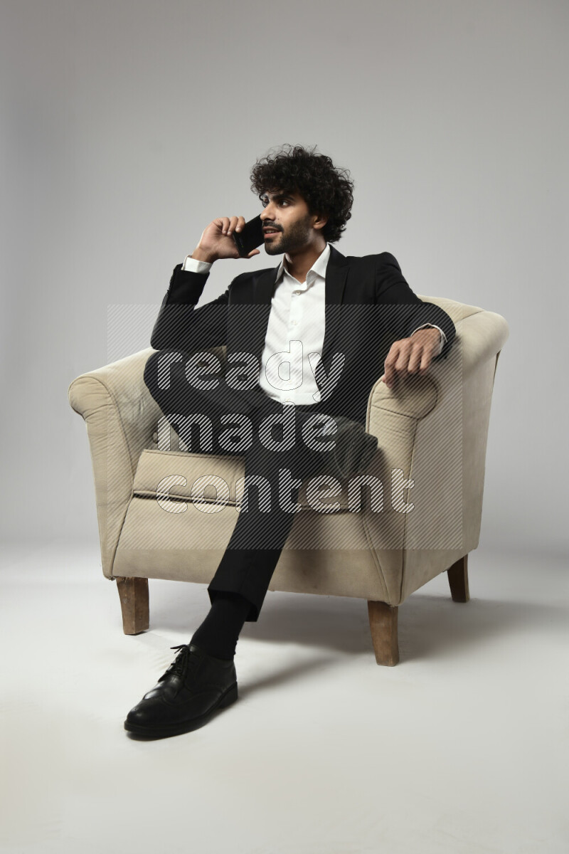 A man wearing formal sitting on a chair talking on the phone on white background