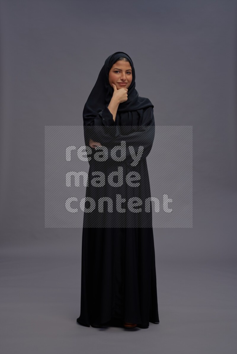 Saudi woman wearing Abaya standing interacting with the camera on gray background