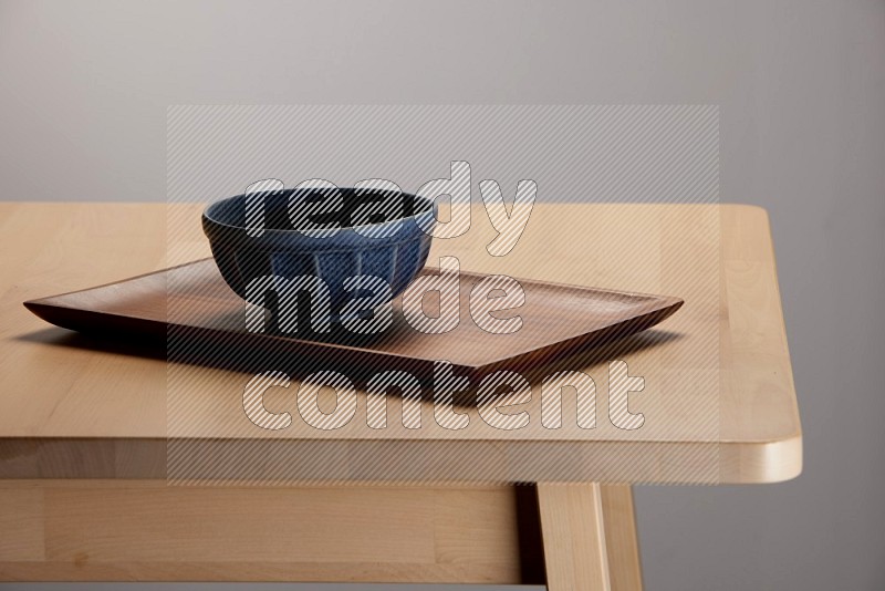blue bowl placed on a rectangular wooden tray on the edge of wooden table