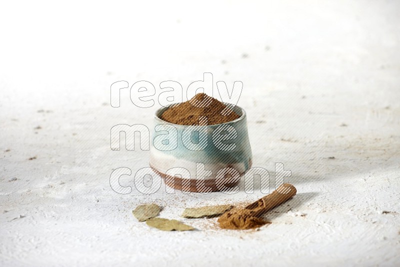 Cinnamon powder in a ceramic bowl with cinnamon sticks and laurel leaves on white background