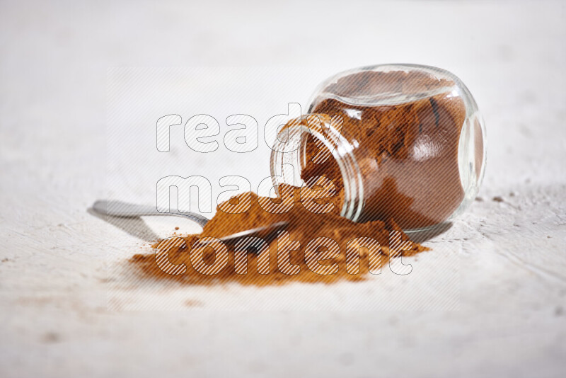 A glass jar full of ground paprika powder flipped with some spilling powder on white background