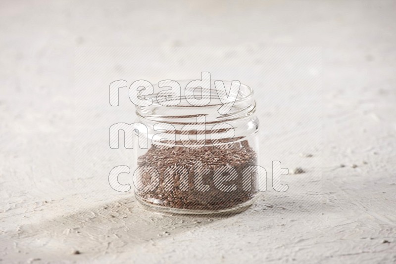 A glass jar full of flax on a textured white flooring in different angles