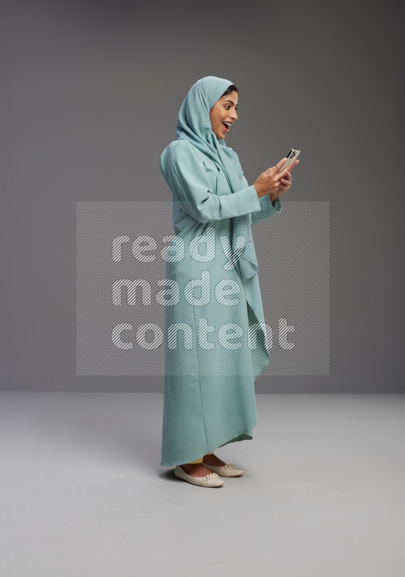 Saudi Woman wearing Abaya standing texting on phone on Gray background