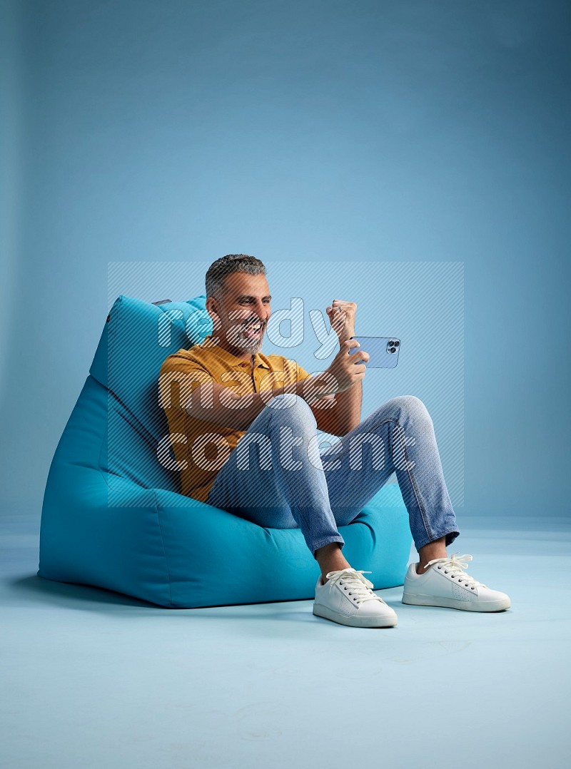 A man sitting on a blue beanbag and playing on phone