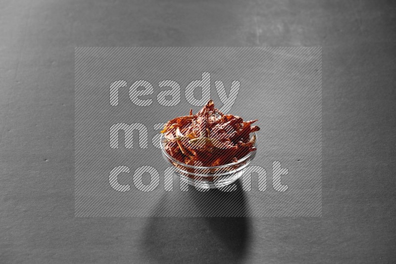 A glass bowl full of dried red chili peppers on black flooring