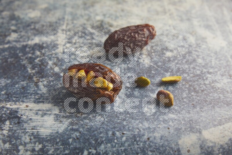 two pistachios stuffed madjoul dates on a rustic blue background