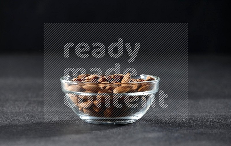 A glass bowl full of peeled almonds on a black background in different angles