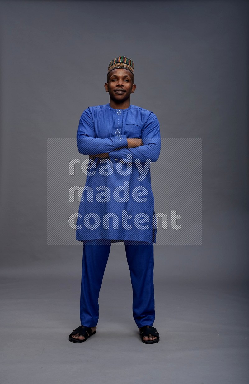 Man wearing Nigerian outfit standing with crossed arms on gray background
