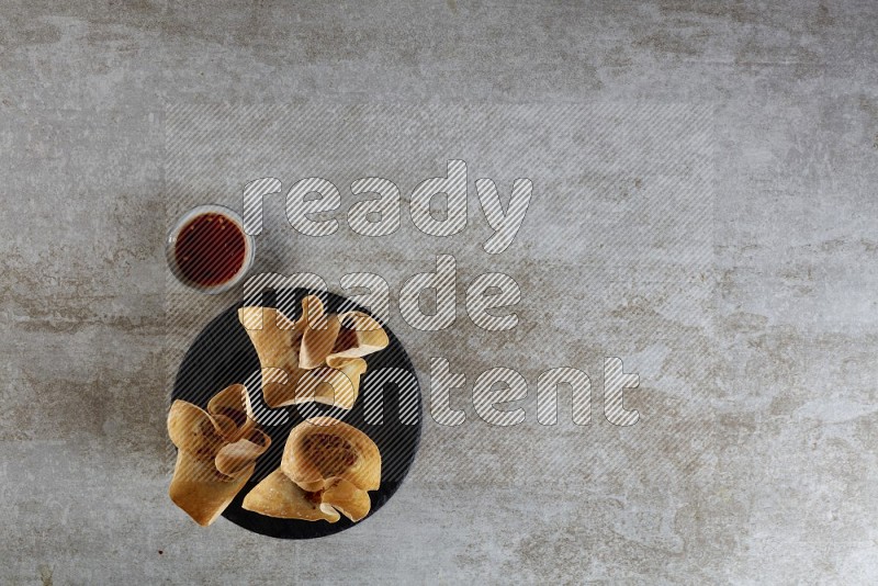 wonton cups with soy sauce ramkin on circle slate on grey textured counter top