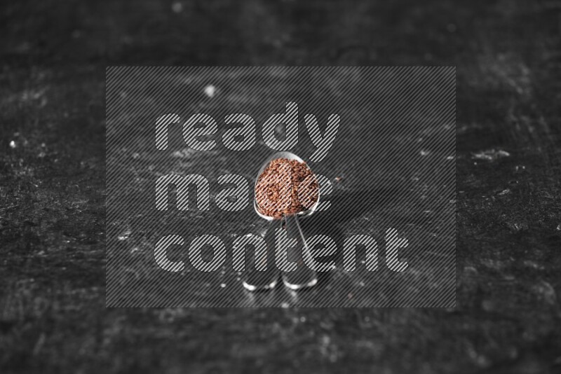 2 metal spoons full of garden cress seeds on a textured black flooring