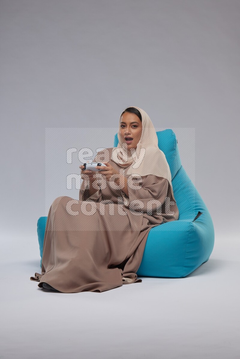 A Saudi woman sitting on a blue beanbag and gaming with joystick