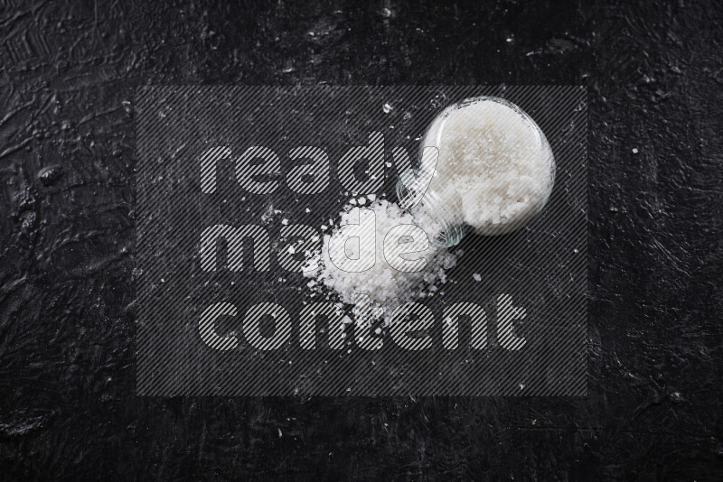 A glass jar full of coarse sea salt crystals on black background