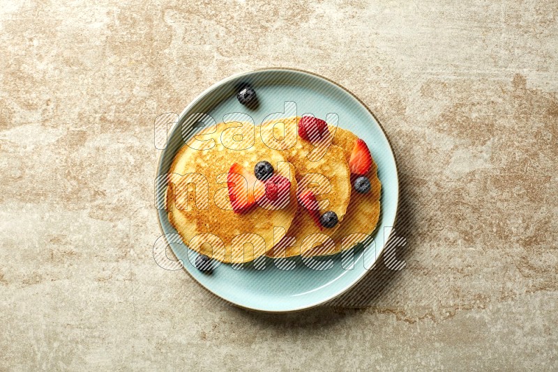 Three stacked mixed berries pancakes in a blue plate on beige background