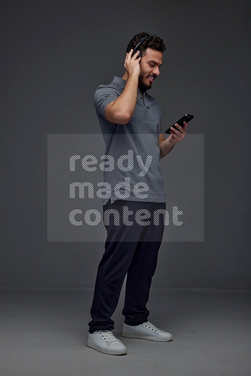 A man wearing casual and using his phone and headphone eye level on a gray background