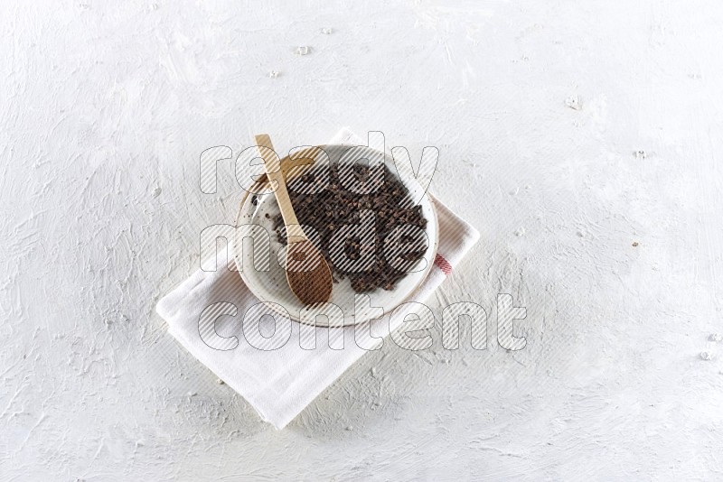 A Pottery plate full of whole cloves and a wooden spoon full of cloves powder in it on a textured white background