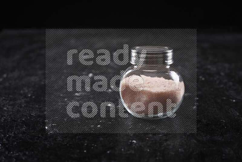 A glass jar full of fine himalayan salt on black background