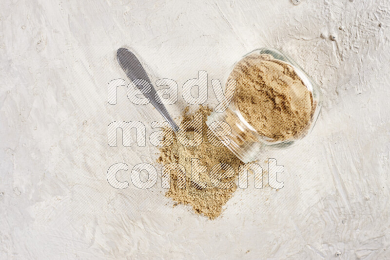 A glass jar full of ground ginger powder flipped with some spilling powder on white background