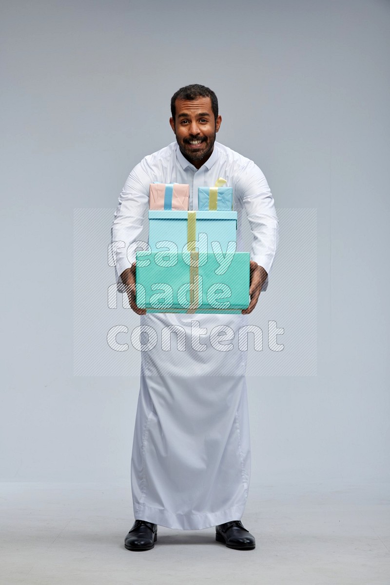 Saudi man Wearing thob standing holding gift box on Gray background