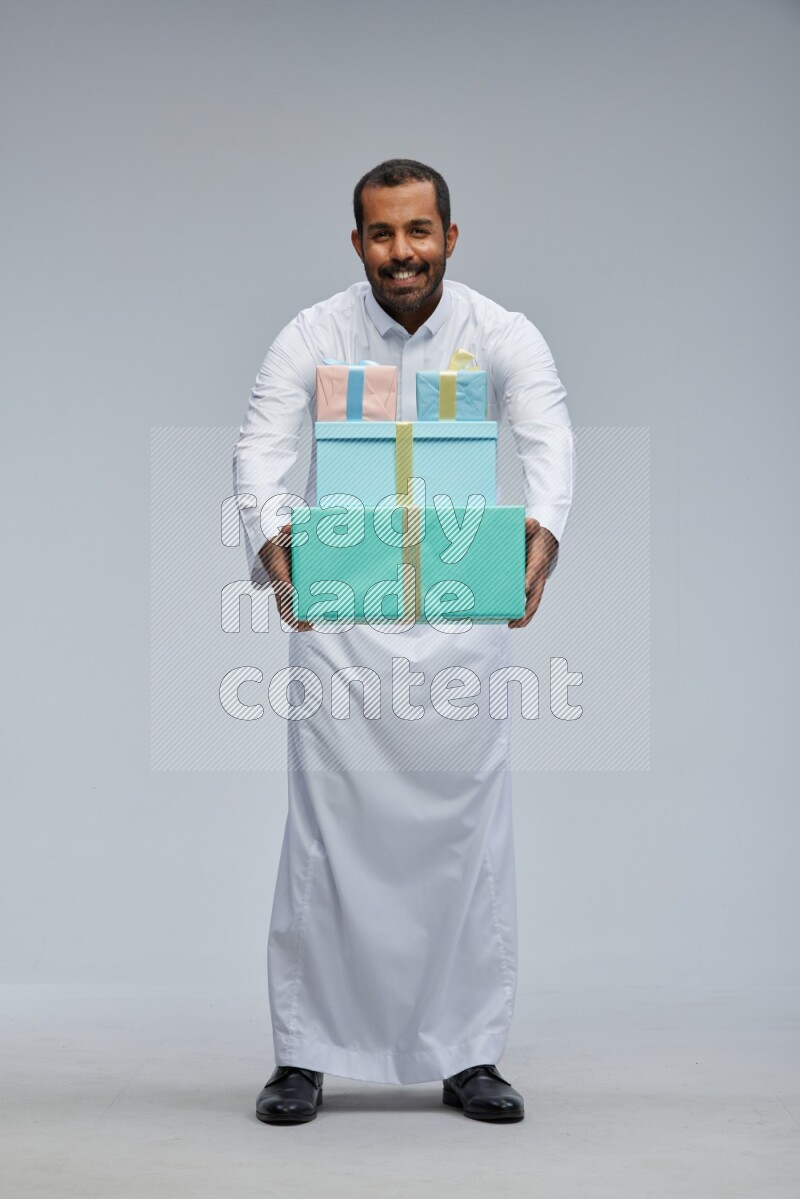 Saudi man Wearing thob standing holding gift box on Gray background